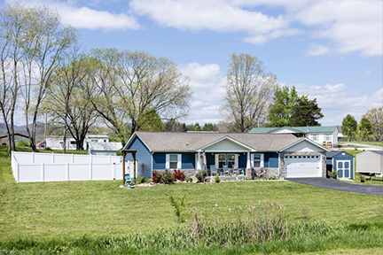 Front view of a blue manufactured home with a shed and fenced backyard