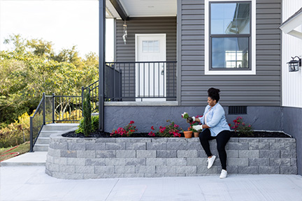 Woman planting flowers in soil behind a retaining wall outside a home