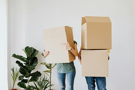 Two people carrying large cardboard moving boxes