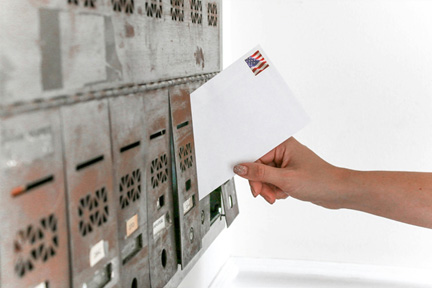 Person with a stamped envelope depositing a letter into a mailbox slot