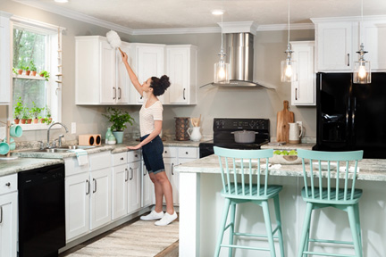 Woman using a duster to clean the top of kitchen cabinetry