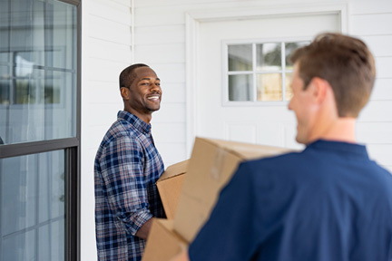 Two men carrying moving boxes by a front door